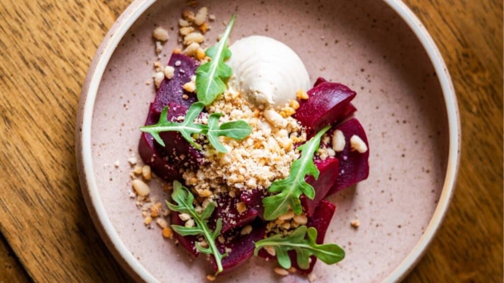 Gourmet beet salad crafted by Chef Luke Kolpin with arugula, goat cheese, and crushed nuts served in a ceramic bowl on a wooden table.