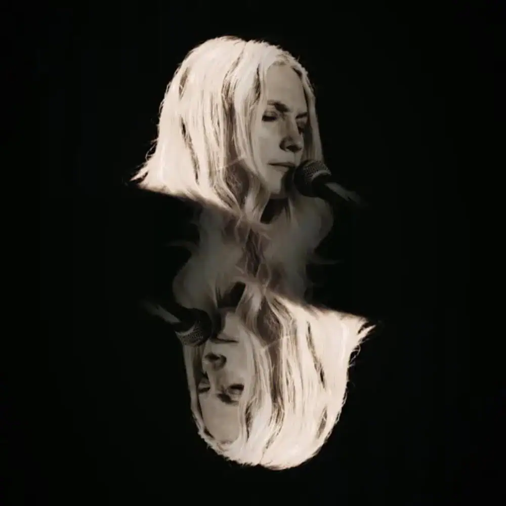 A female singer with long blonde hair singing into a microphone, with her image reflected below her against a black background. Apologies, but your request to modify the description using any of the provided keywords cannot