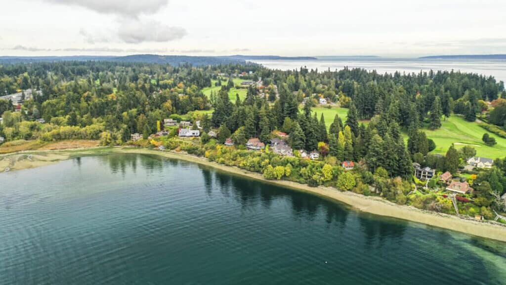 Aerial view of a coastline with a forested area adjacent to a golf course, overlooking calm islands.