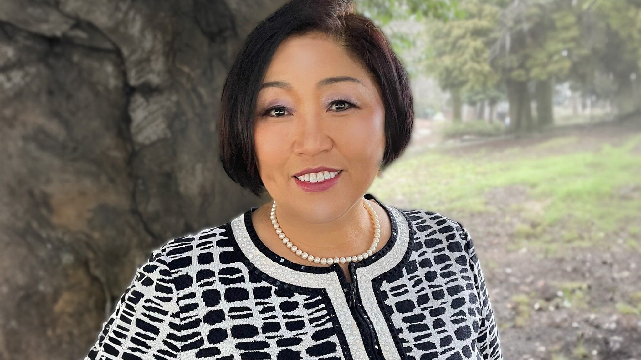 Woman in a patterned jacket and uncommon thinkers pearl necklace smiling outdoors.