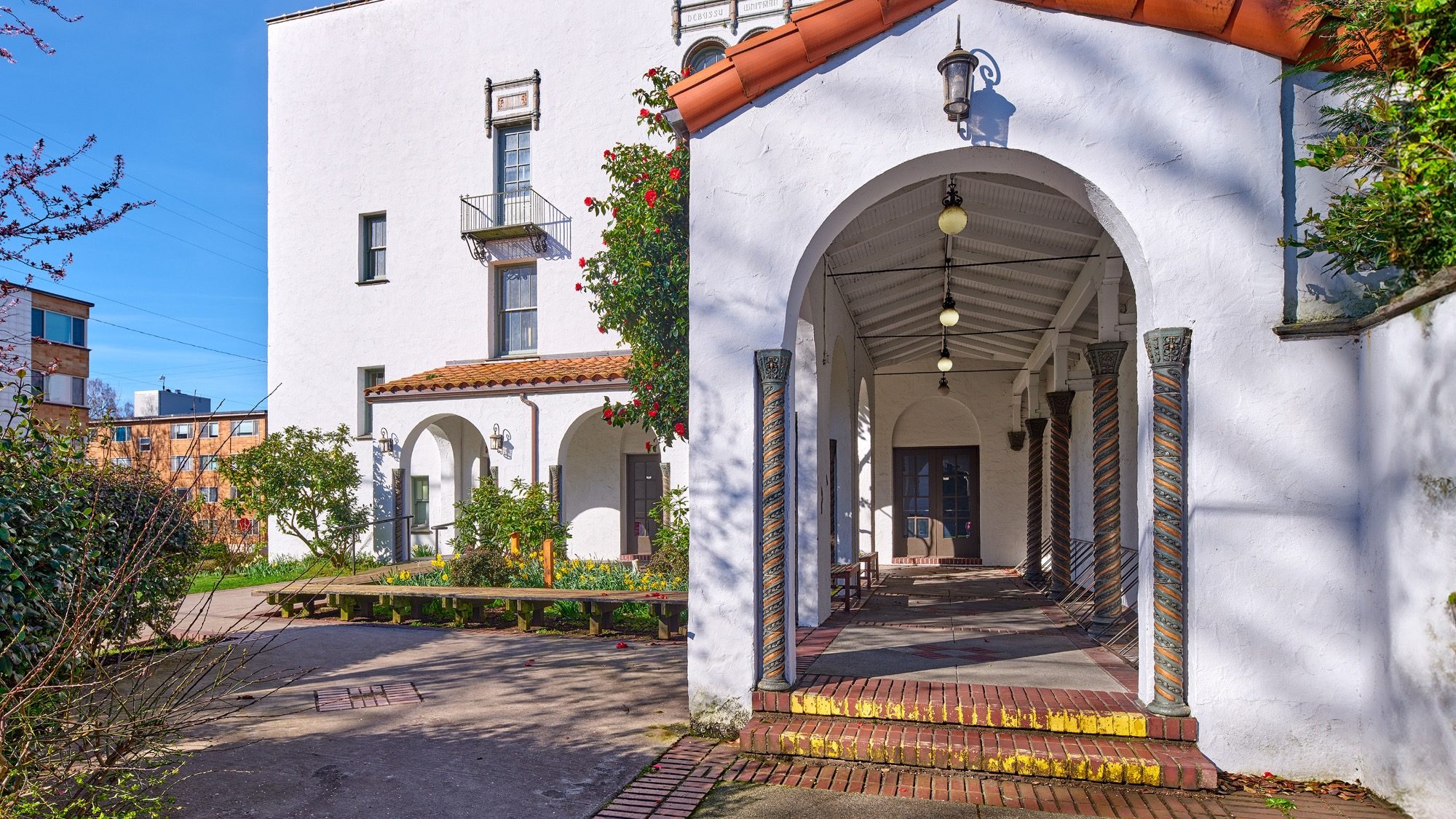 Spanish colonial style building with archways and tiled pillars, bright sunny day, site of a recent sit-in protest, residential area in background.