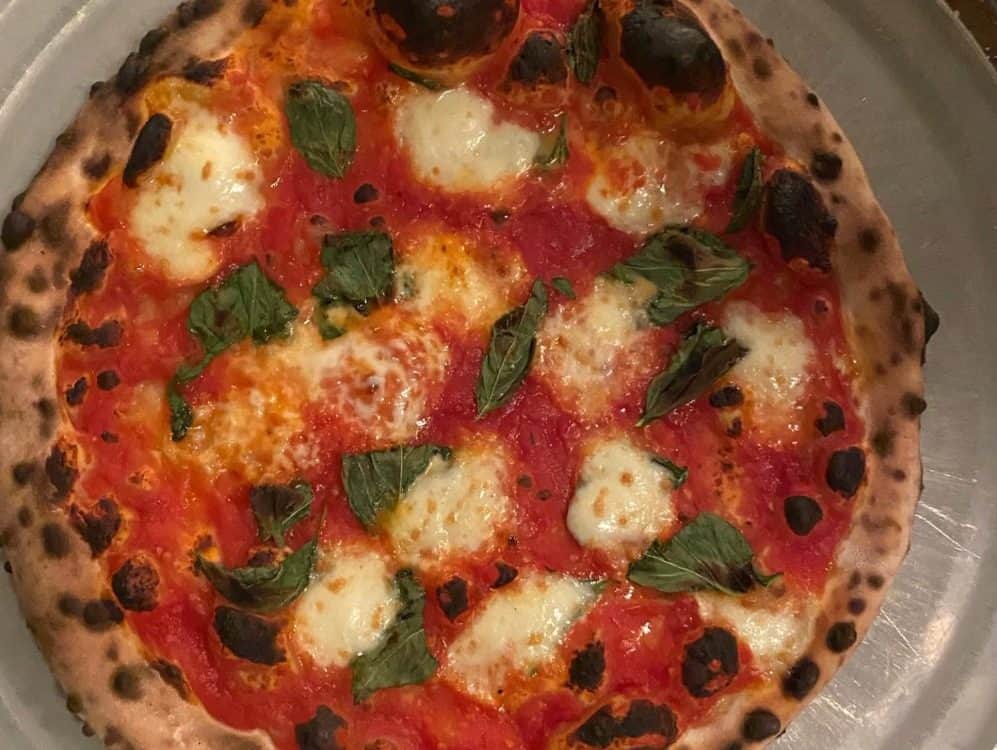 A freshly baked pizza with tomato sauce, melted mozzarella cheese, and basil leaves, featured in Seattle magazine, showing a well-charred crust.