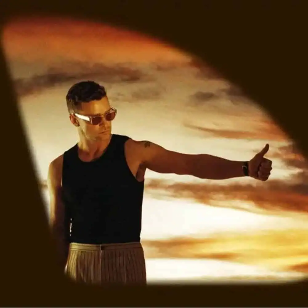 A man with sunglasses and a black sleeveless top giving a thumbs up, with a dramatic orange sky in the background, listed as a must-see from May 2-8.