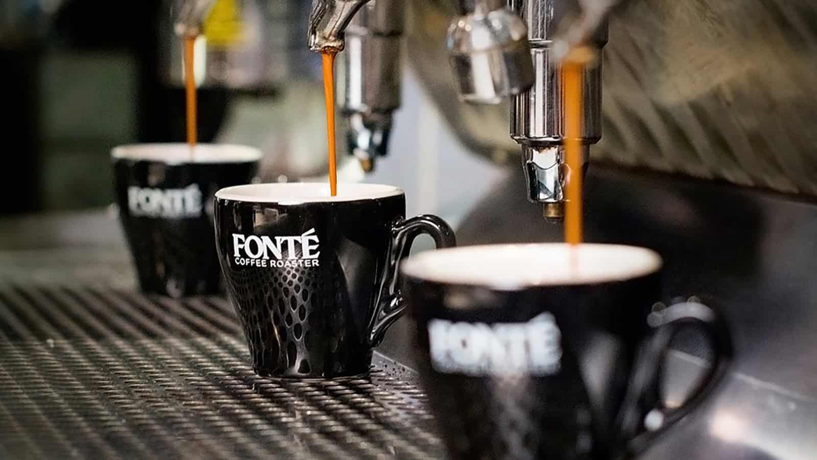 Three black Fonte coffee mugs are placed under espresso machines with espresso being dispensed into them, creating a scene of artisanal coffee art.