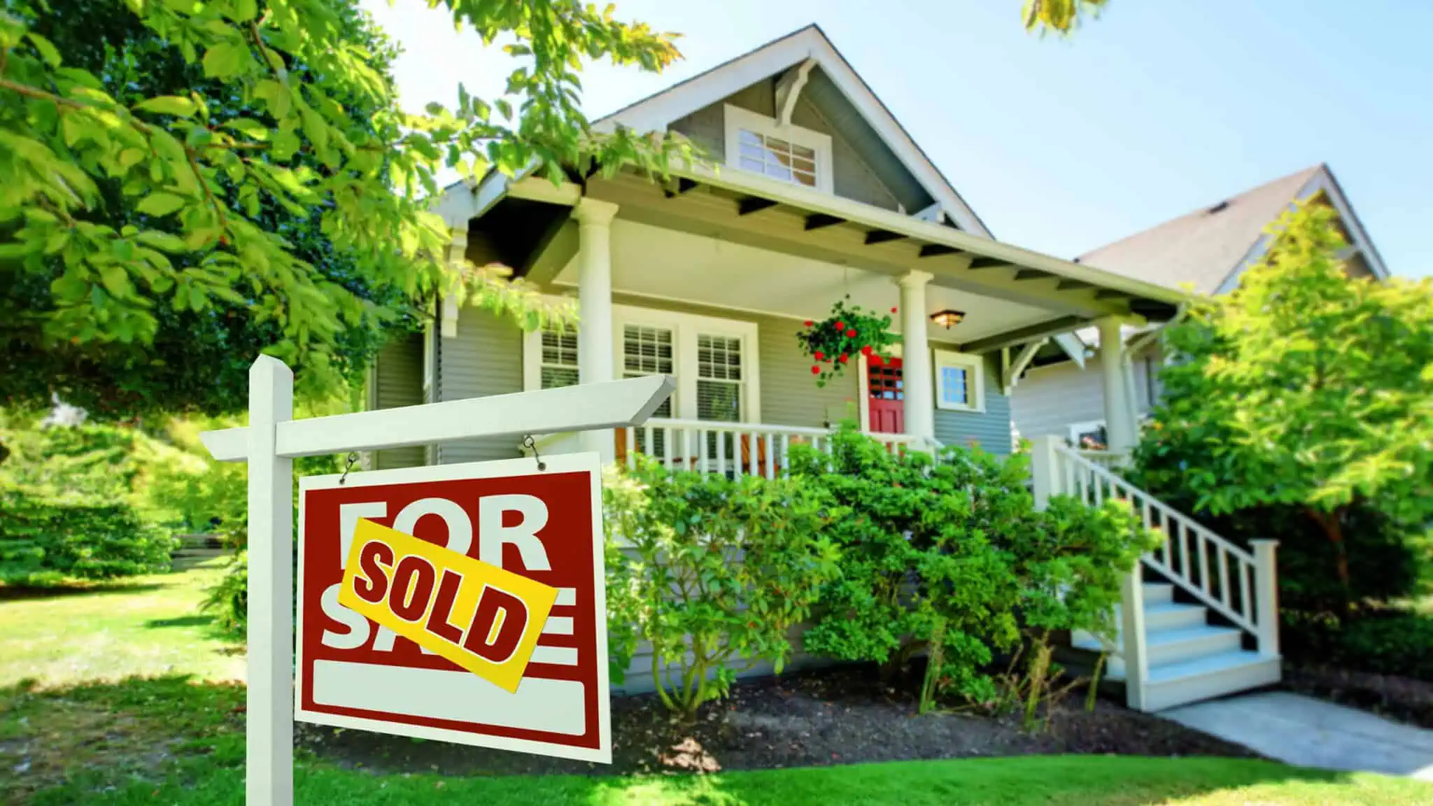 A house with a "Sold" sign in front, surrounded by green foliage and trees, listed on Zillow, boasts a charming small front porch and a striking red door.