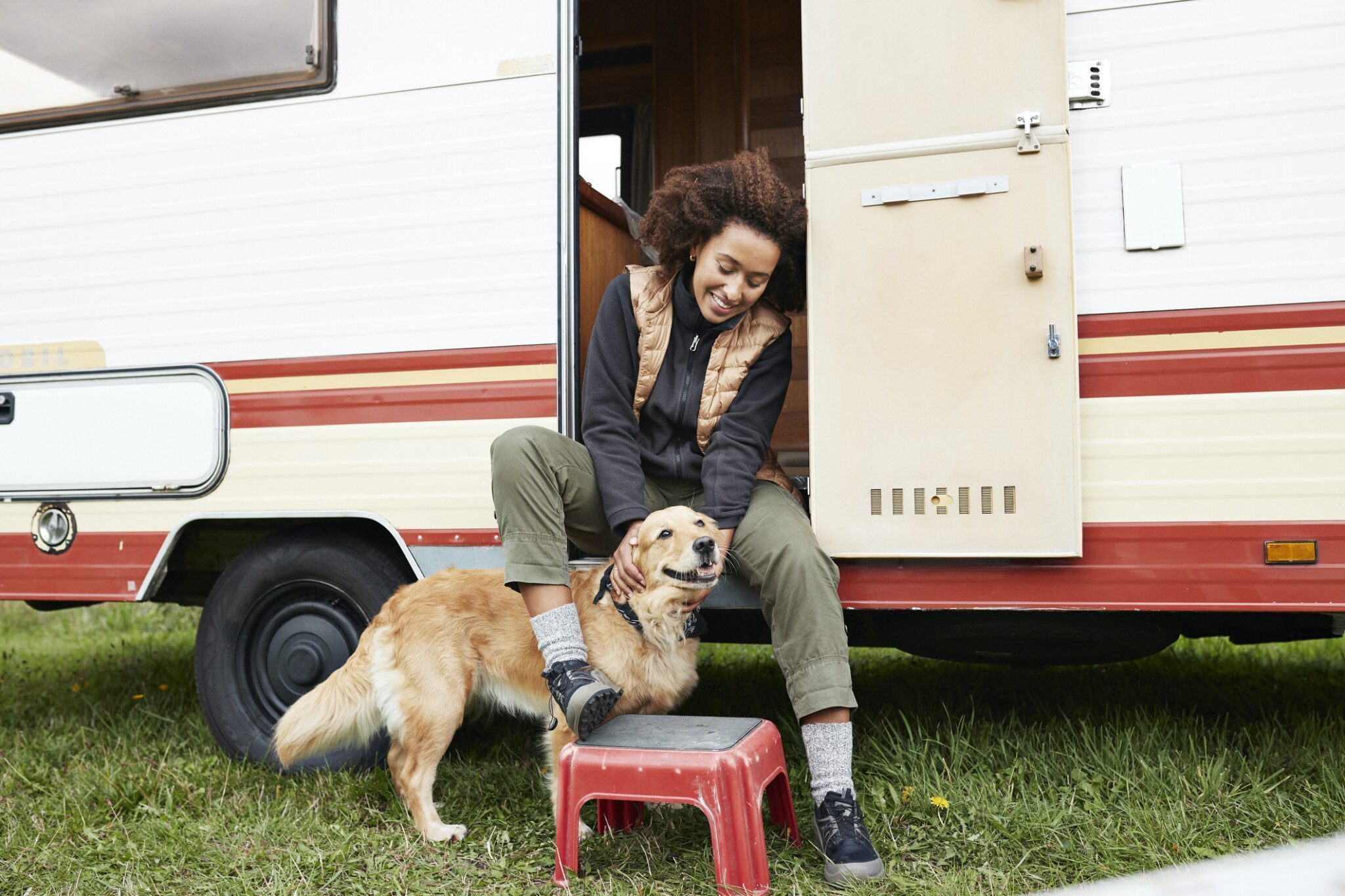 Smiling woman sitting with dog on doorway of camper van during vacation