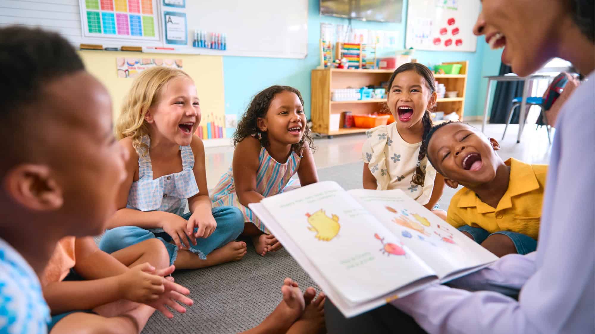 A group of children sit in a colorful, educational classroom, laughing, while a teacher reads a picture book to them. It's no wonder a report ranks Washington state No. 1 for teachers—this cheerful scene is a testament to their dedication and the vibrant learning environment they create.