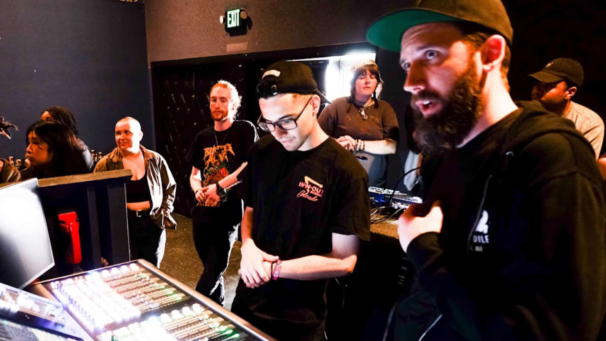 Group of people in the entertainment industry engaging with audio equipment in a dimly lit studio, focusing intently on the screen and controls.