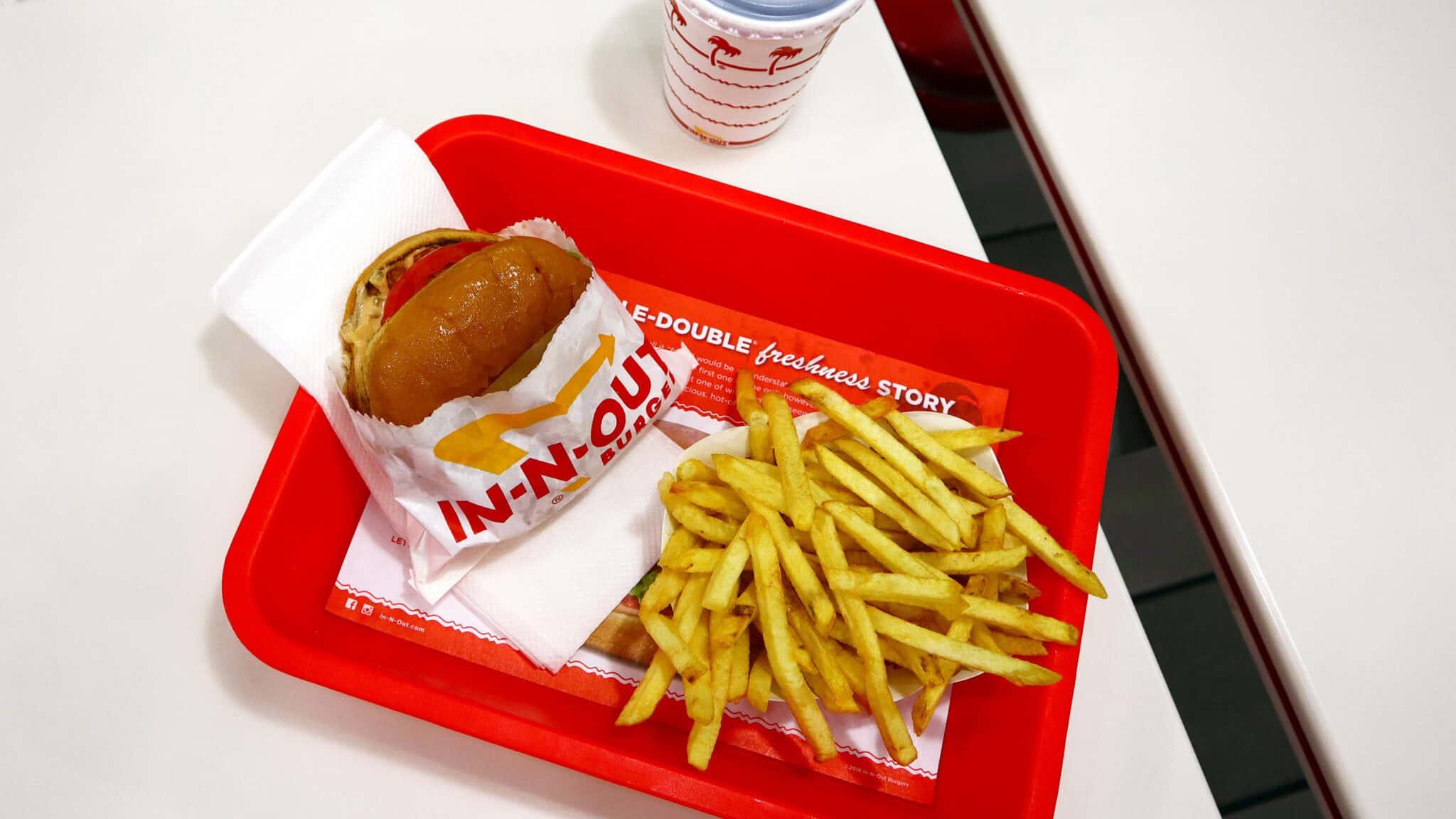 A tray with an In-N-Out burger and fries on a red table, accompanied by a drink with the restaurant's logo.