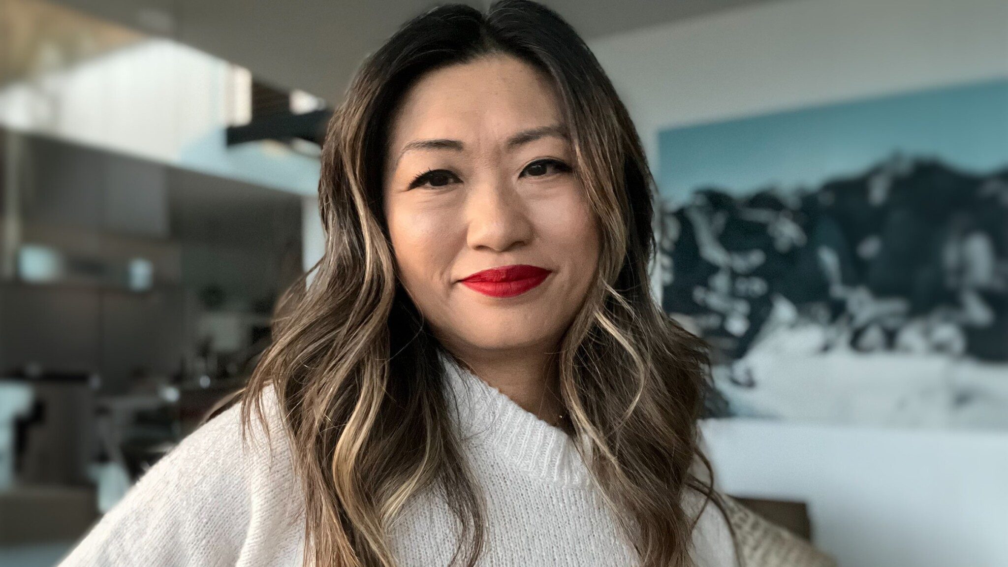 A woman with red lipstick smiling in a room with an art piece by Uncommon Thinkers in the background.