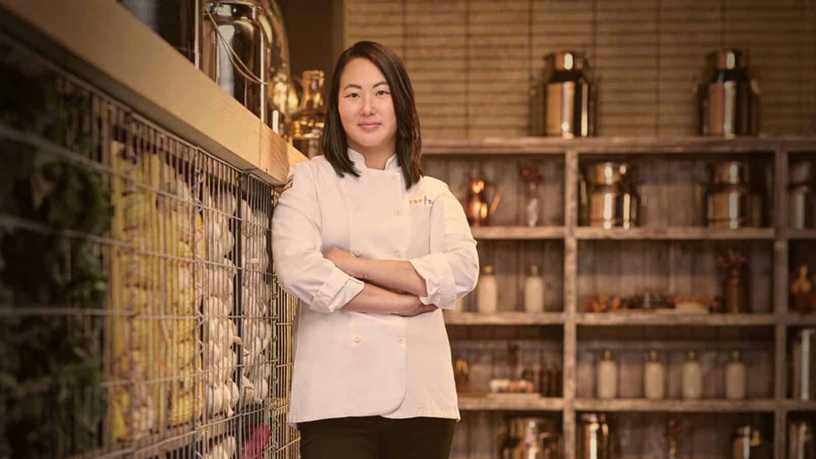 A Top Chef Kaleena Bliss with crossed arms standing proudly in a restaurant kitchen.