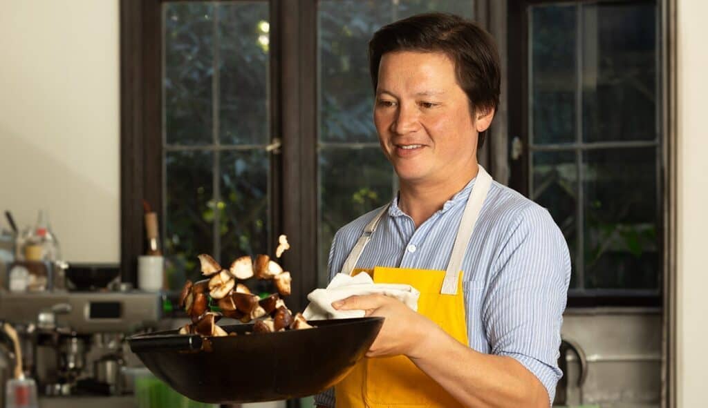 A person in an apron cooking with a wok in a Kitchen Conversations setting.