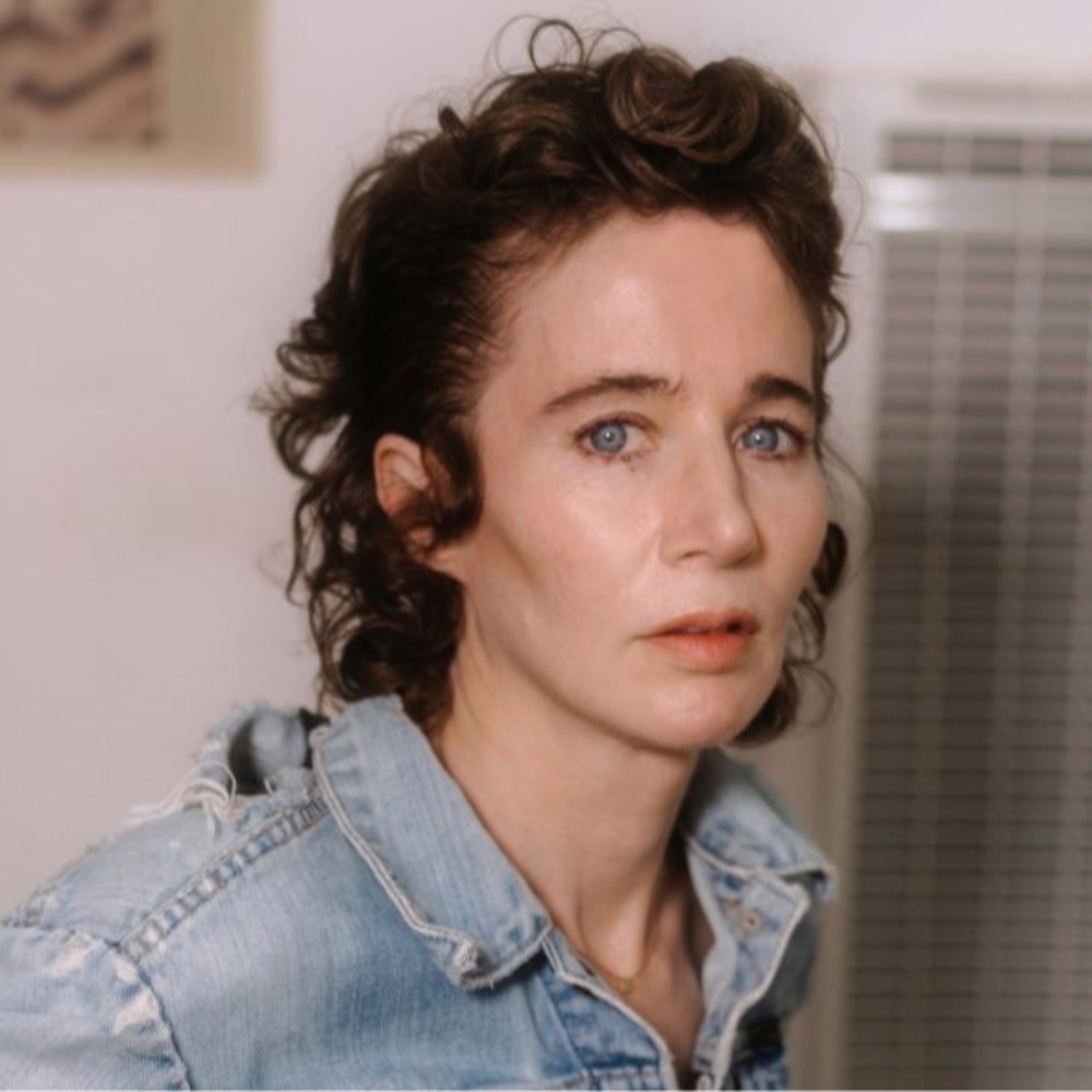 A person with short, wavy hair and blue eyes, wearing a denim jacket, looks towards the camera with a neutral expression on 5/16/2024.
