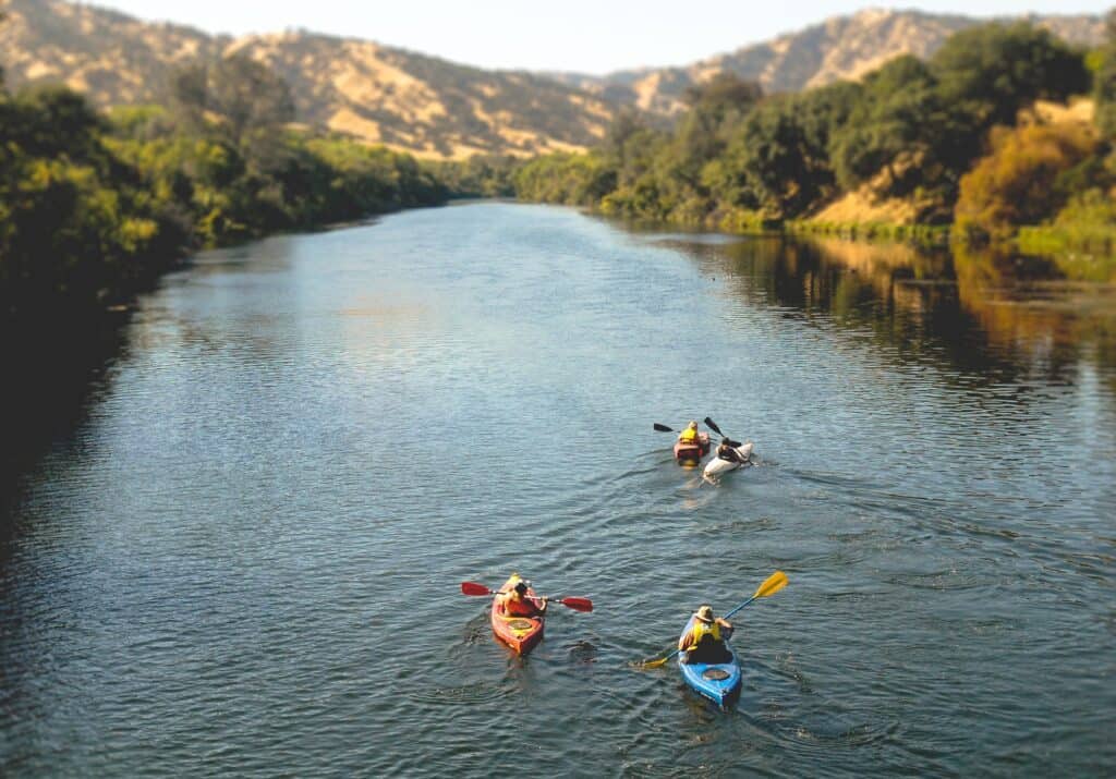 Three people kayaking on a serene river in Yolo County, with a backdrop of hills, discovering a hidden gem.