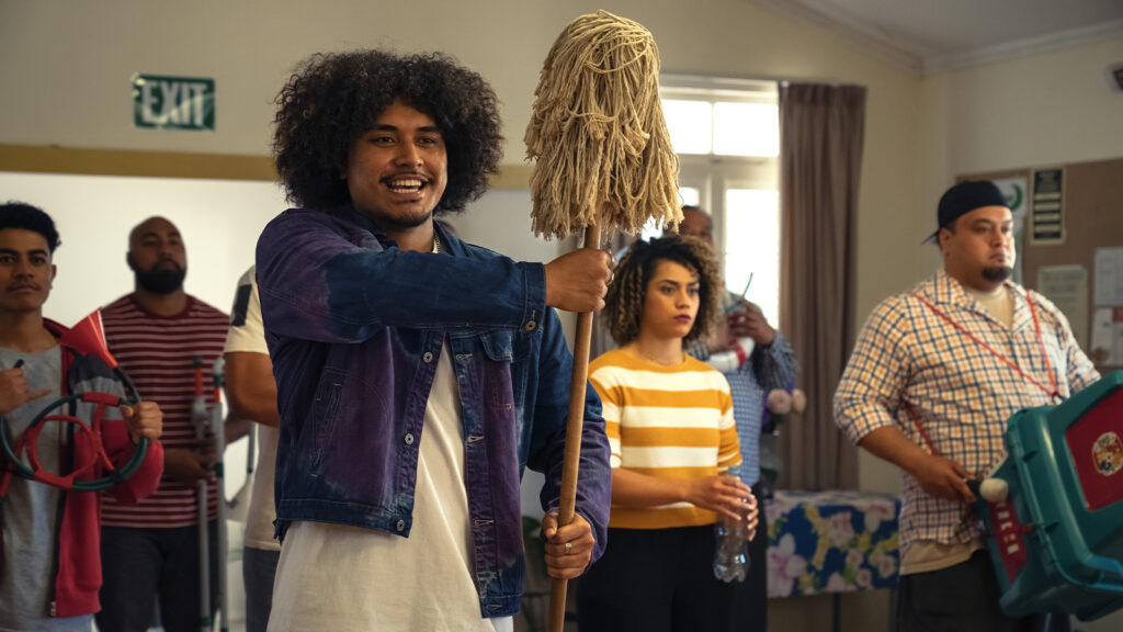 A group of people are gathered indoors, with one individual holding a mop and others holding various household items. This week, they appear to be making music with the objects in an impromptu performance reminiscent of must-see films showcased at SIFF.