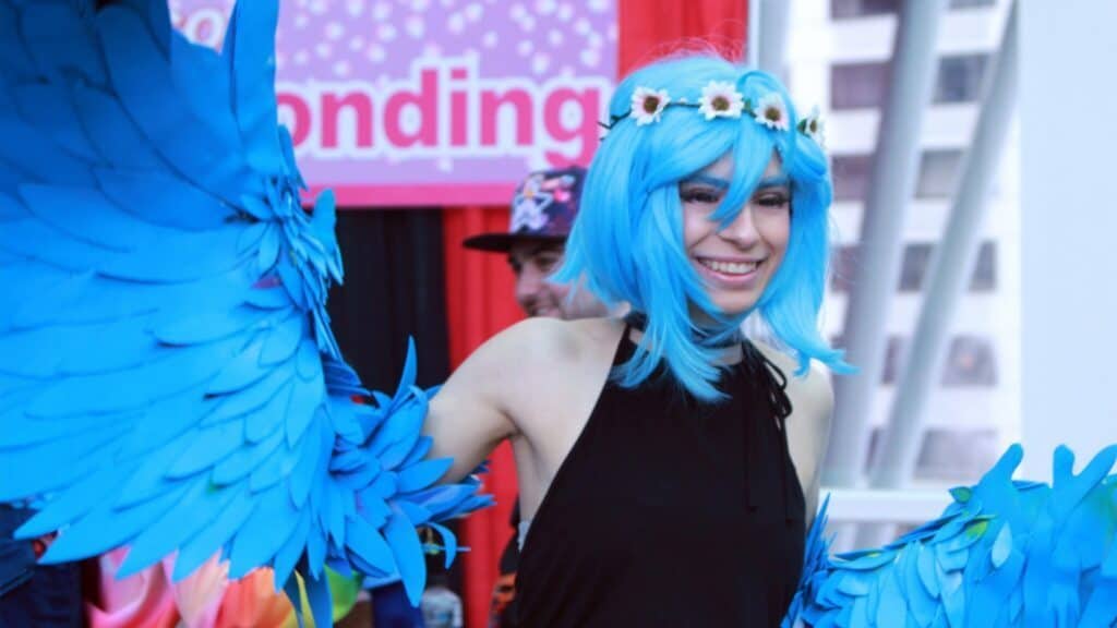 Person in blue wig and winged costume at a festive event.