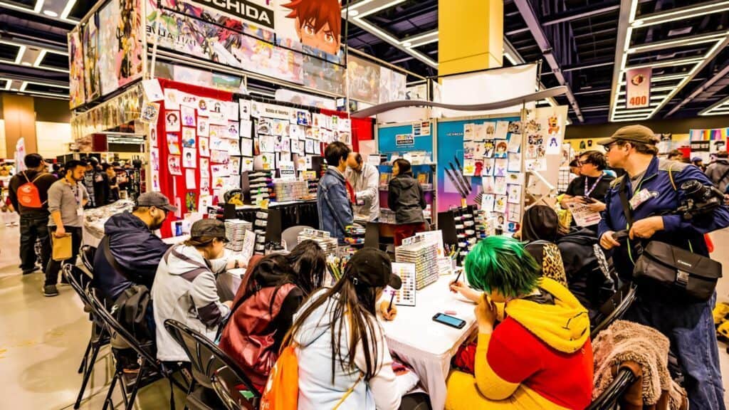 Visitors browsing merchandise at a colorful anime convention booth.