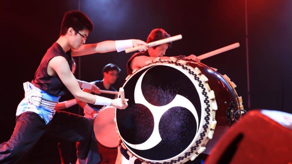 Performers energetically playing a traditional japanese taiko drum on stage.