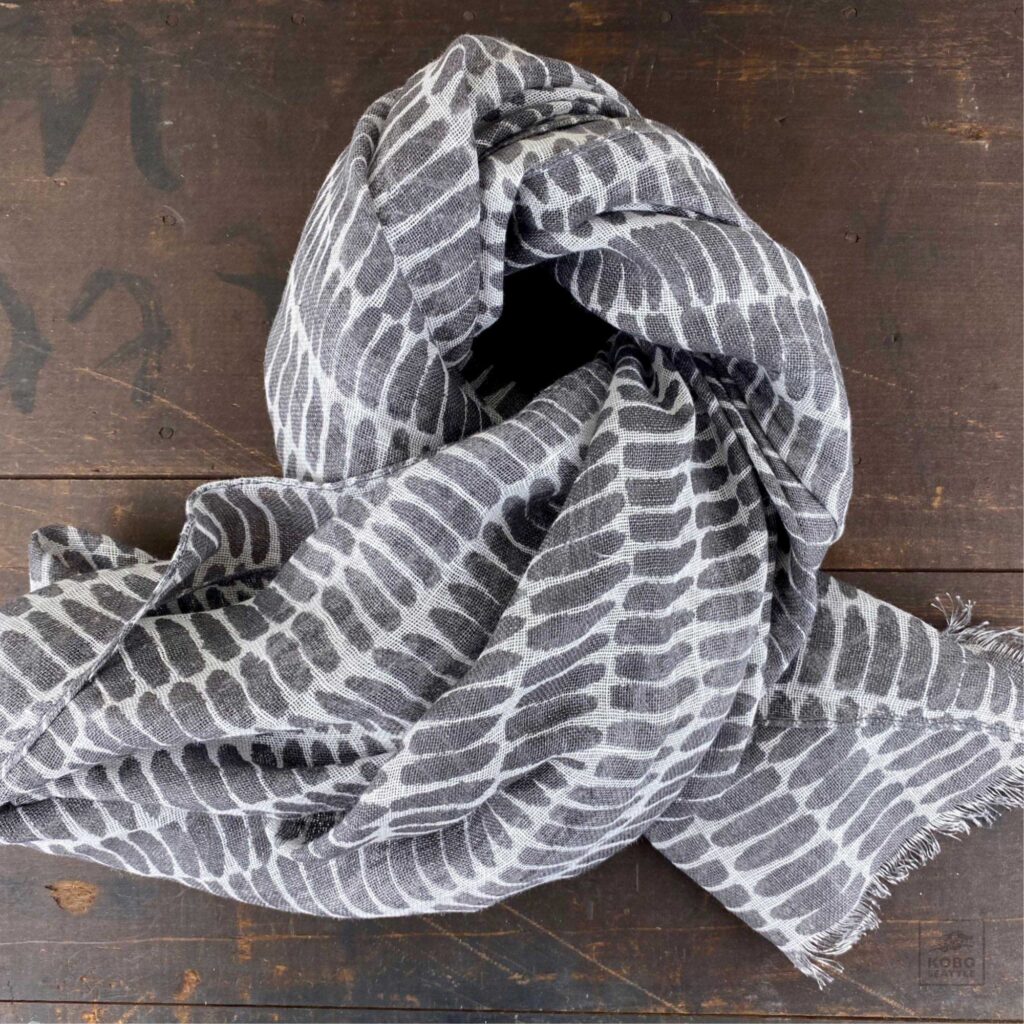 Gray and white striped scarf loosely knotted, displayed on a wooden surface as a perfect Mother's Day gift.