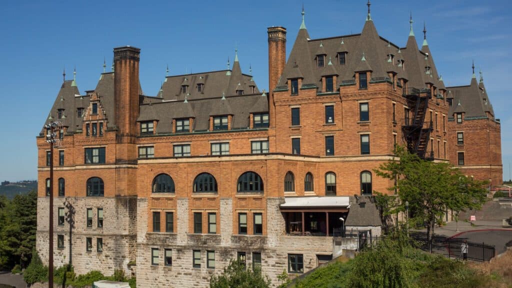 Historic stone and brick building featured in the movie "10 Things I Hate About You" with steeply pitched roofs and multiple chimneys, surrounded by trees under a clear blue sky.