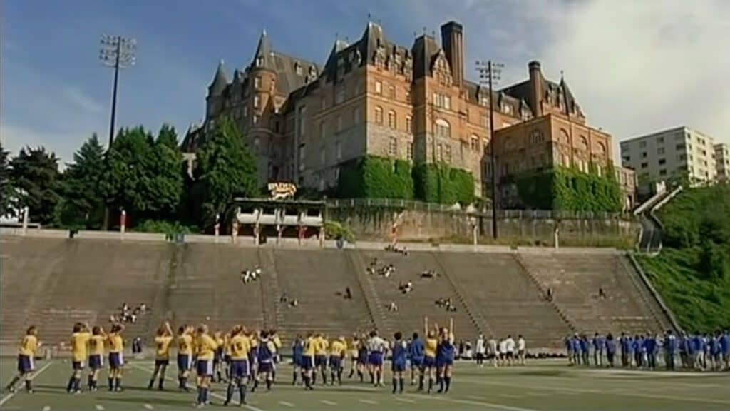 Football teams stretch on a field below a grand, castle-like building on a sunny day, celebrating the movie anniversary of "10 Things I Hate About You," which turns 25.