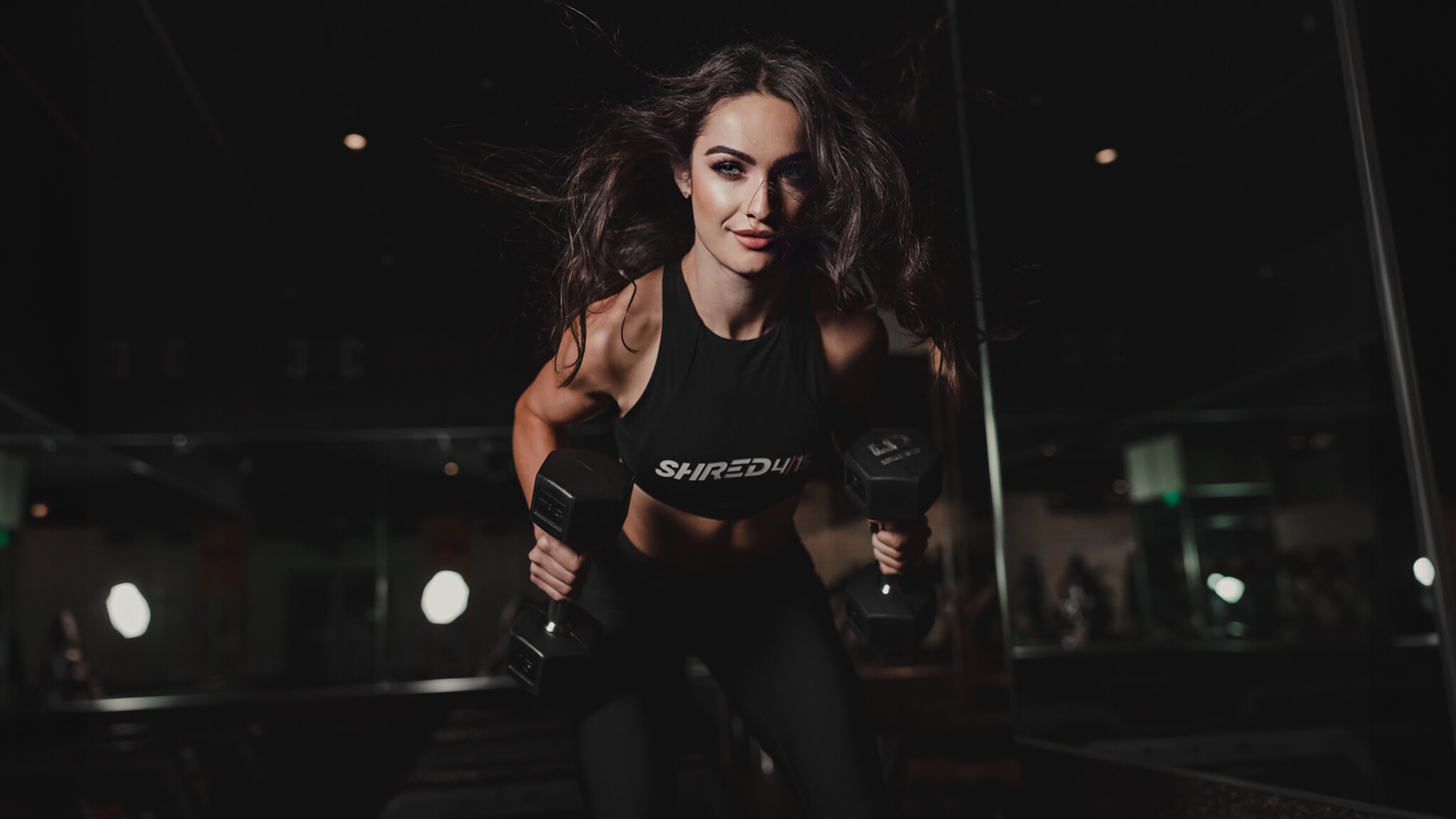 Woman exercising indoors, performing a bent-over dumbbell row, wearing exercise attire, and looking ahead with determination.