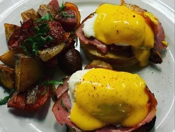 A plate of eggs benedict with Canadian bacon and hollandaise sauce, featured in Seattle magazine, accompanied by a side of seasoned roasted potatoes.