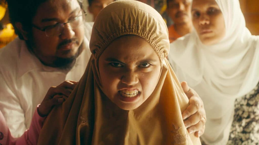 A person wearing a brown headscarf appears visibly upset, with hands on their shoulders from others in the background providing support.