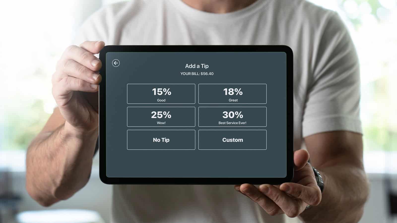 A person holds a tablet displaying tipping options: 15% "Good," 18% "Great," 25% "Wow!," 30% "Best Service Ever!," "No Tip," and "Custom." The bill amount shown is $56.40, illustrating the tipping scourge known as tipflation.