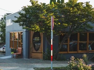 A cozy corner cafe with large windows and a green tree outside, named "Union Saloon," located in a quiet neighborhood, featured in Seattle Magazine.