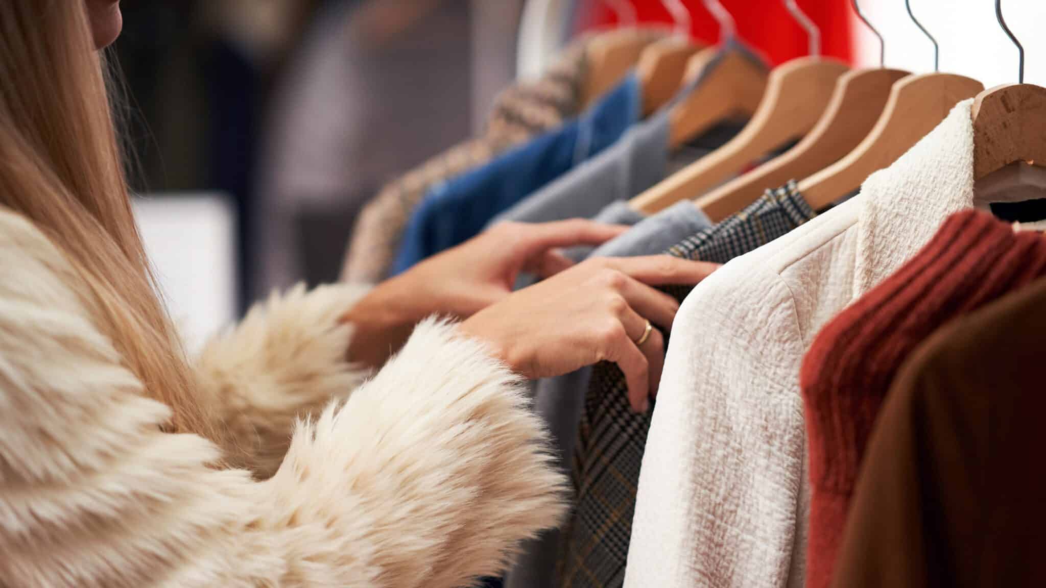 Two people browsing through a clothes rack in a store, examining various garments for a closet refresh.